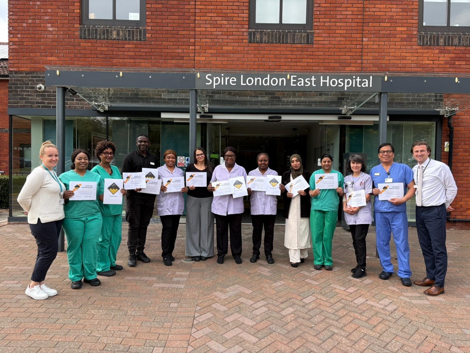 Housekeeping and hospital staff at Spire London East Hospital celebrating their third consecutive Gold CAP Award outside the hospital entrance.