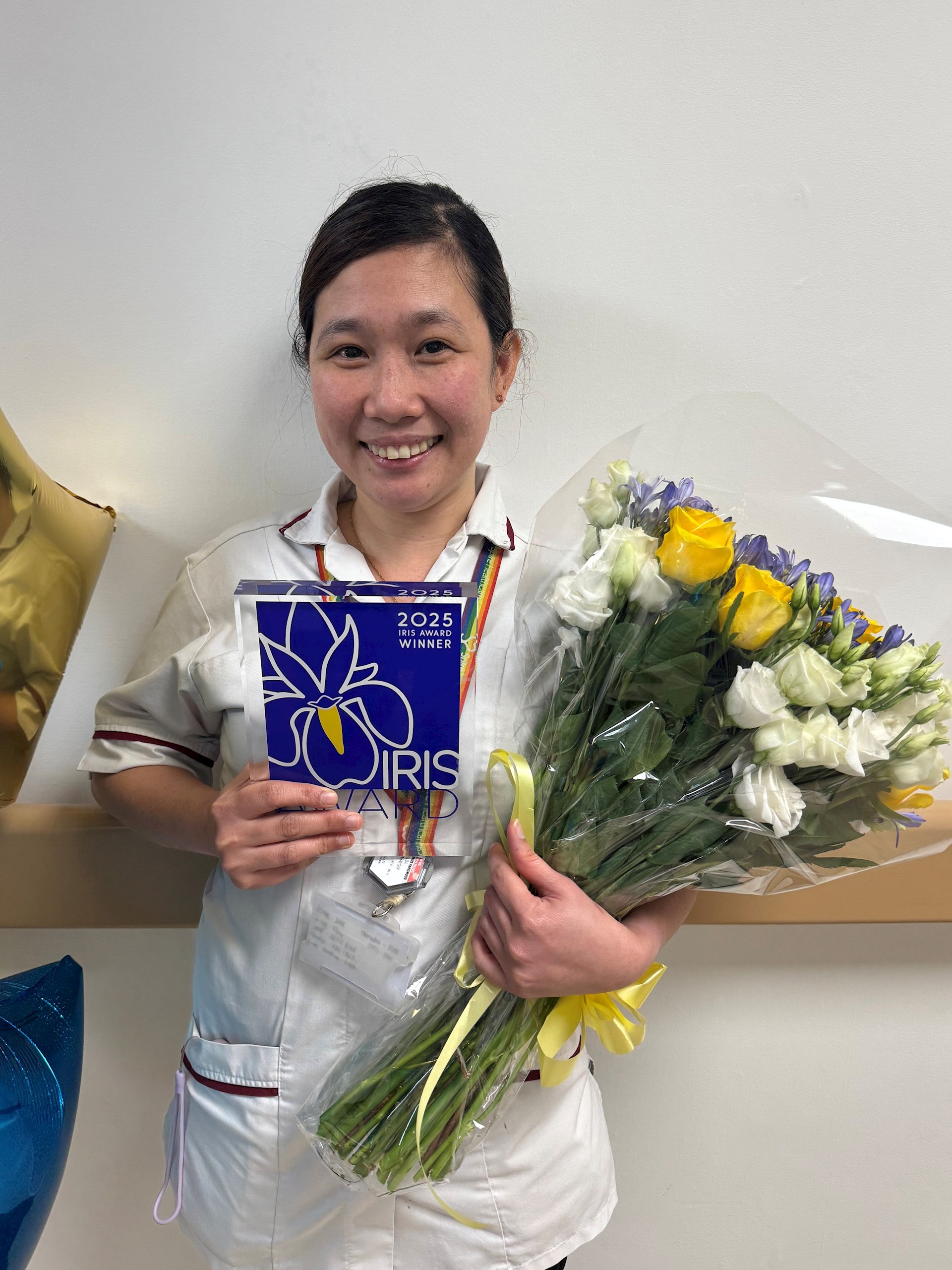 Hilda Garaygay, a speciality radiographer at Spire Hartswood Hospital, holding her 2025 IRIS Award and a bouquet of flowers.