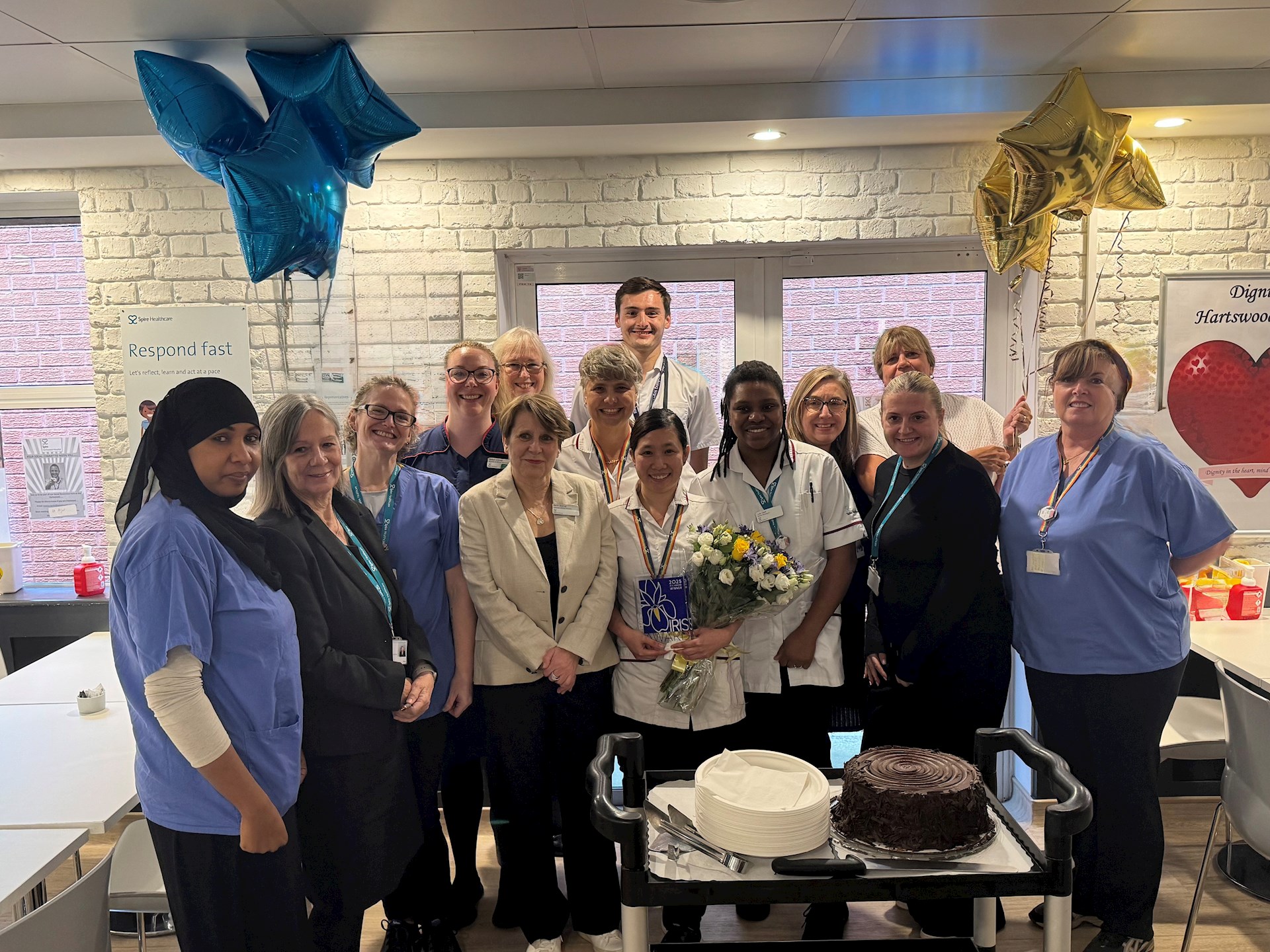 Hilda Garaygay with colleagues at Spire Hartswood Hospital celebrating her 2025 IRIS Award, surrounded by balloons and a celebration cake.